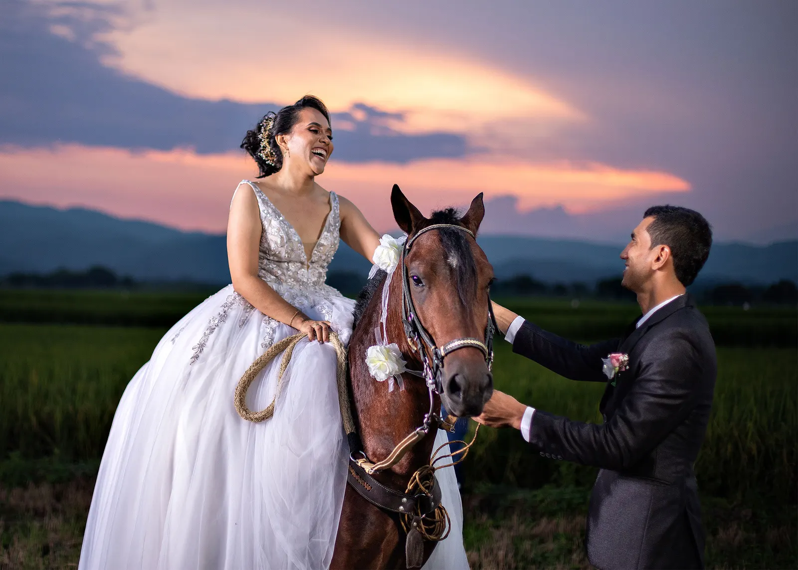 Novia riendo sobre un caballo junto al novio al atardecer