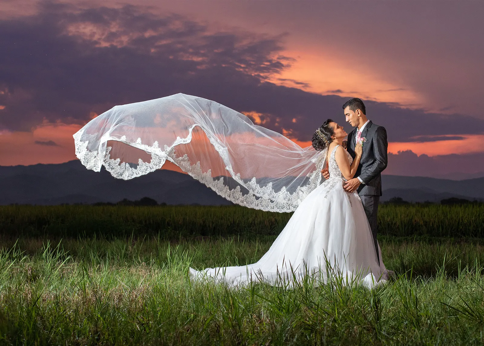 Novios abrazados con el velo al viento en un atardecer