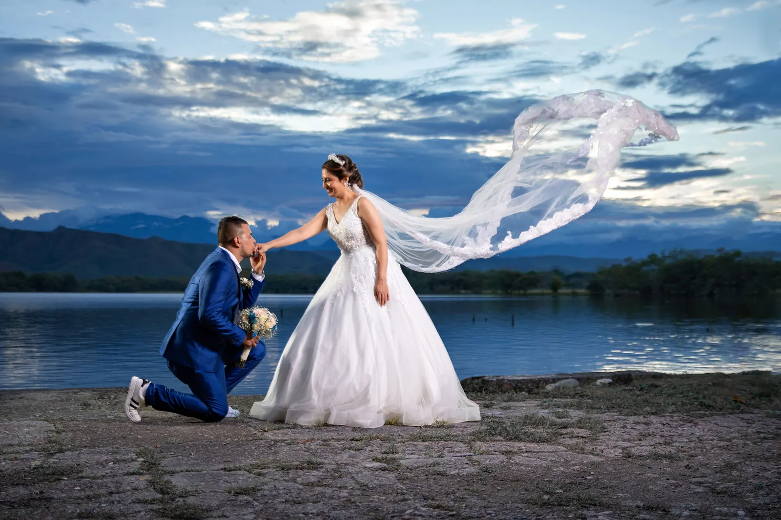 Novio besando la mano de la novia junto a un lago