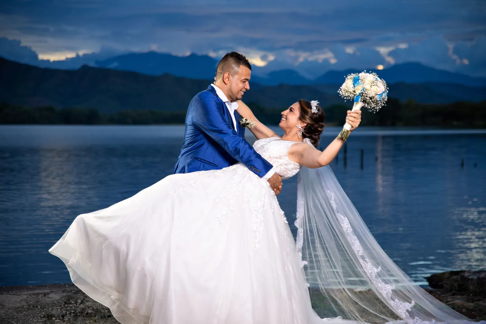 Novios bailando junto al lago con ramo de flores