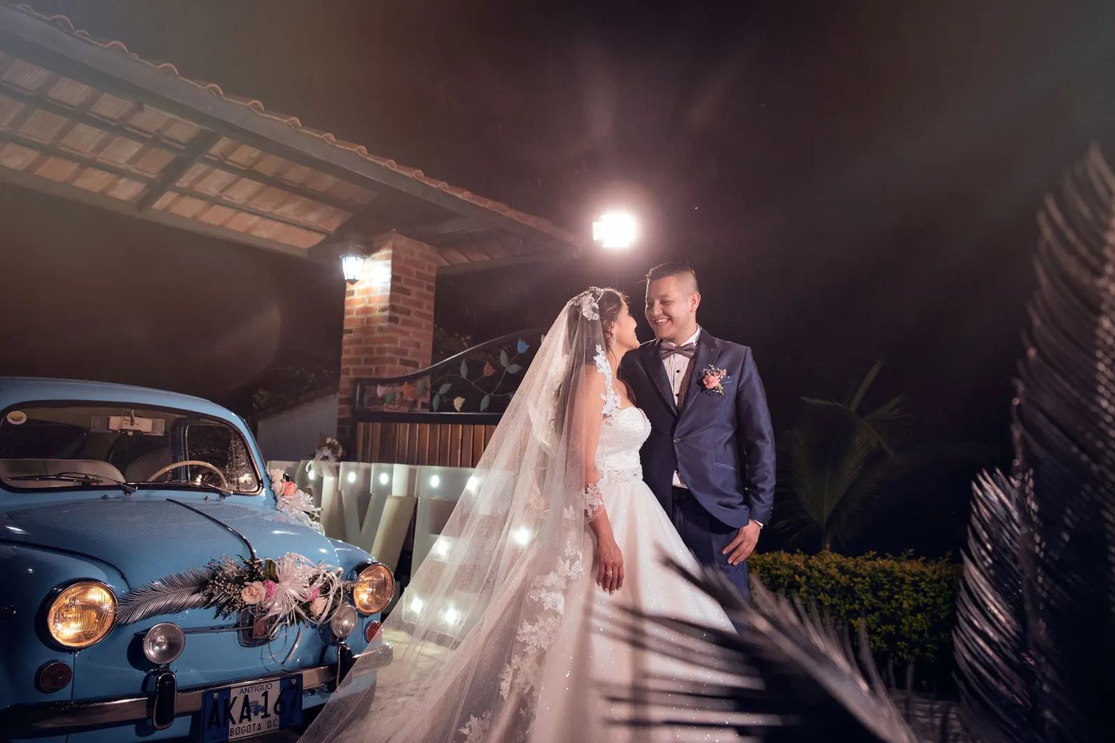 Novios junto a un auto clásico azul de noche