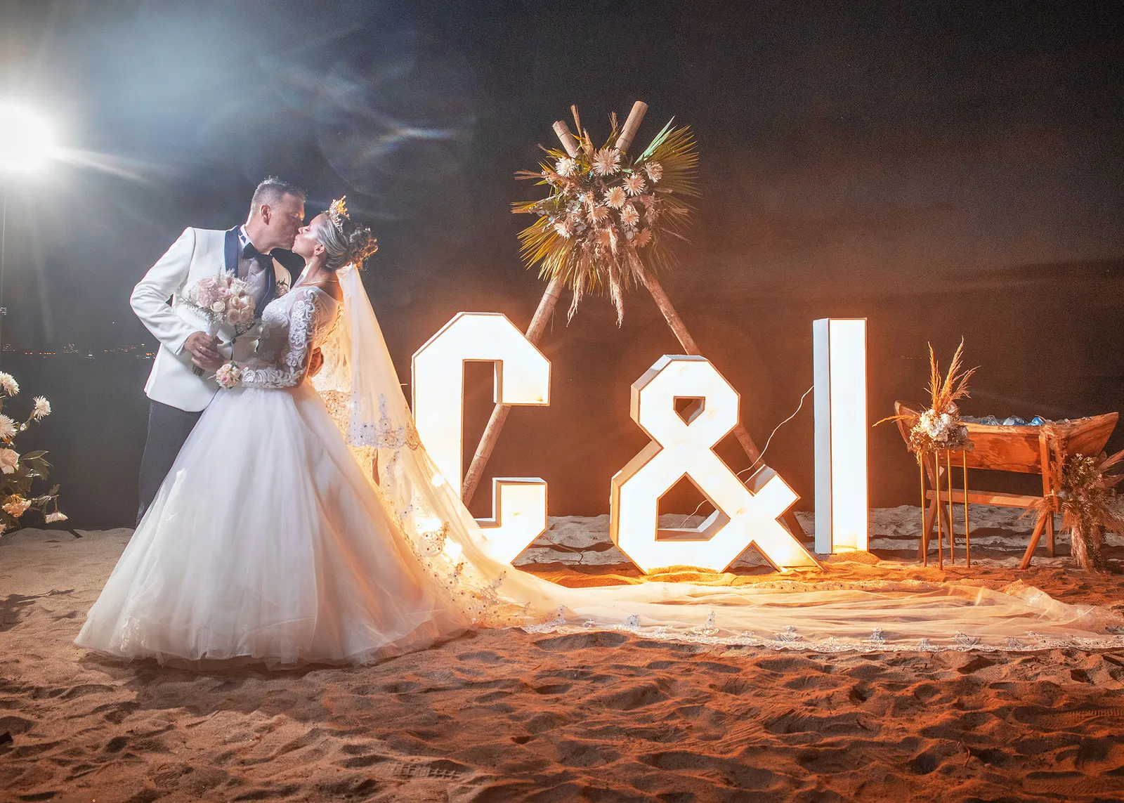 Novios besándose junto a letras iluminadas en la playa