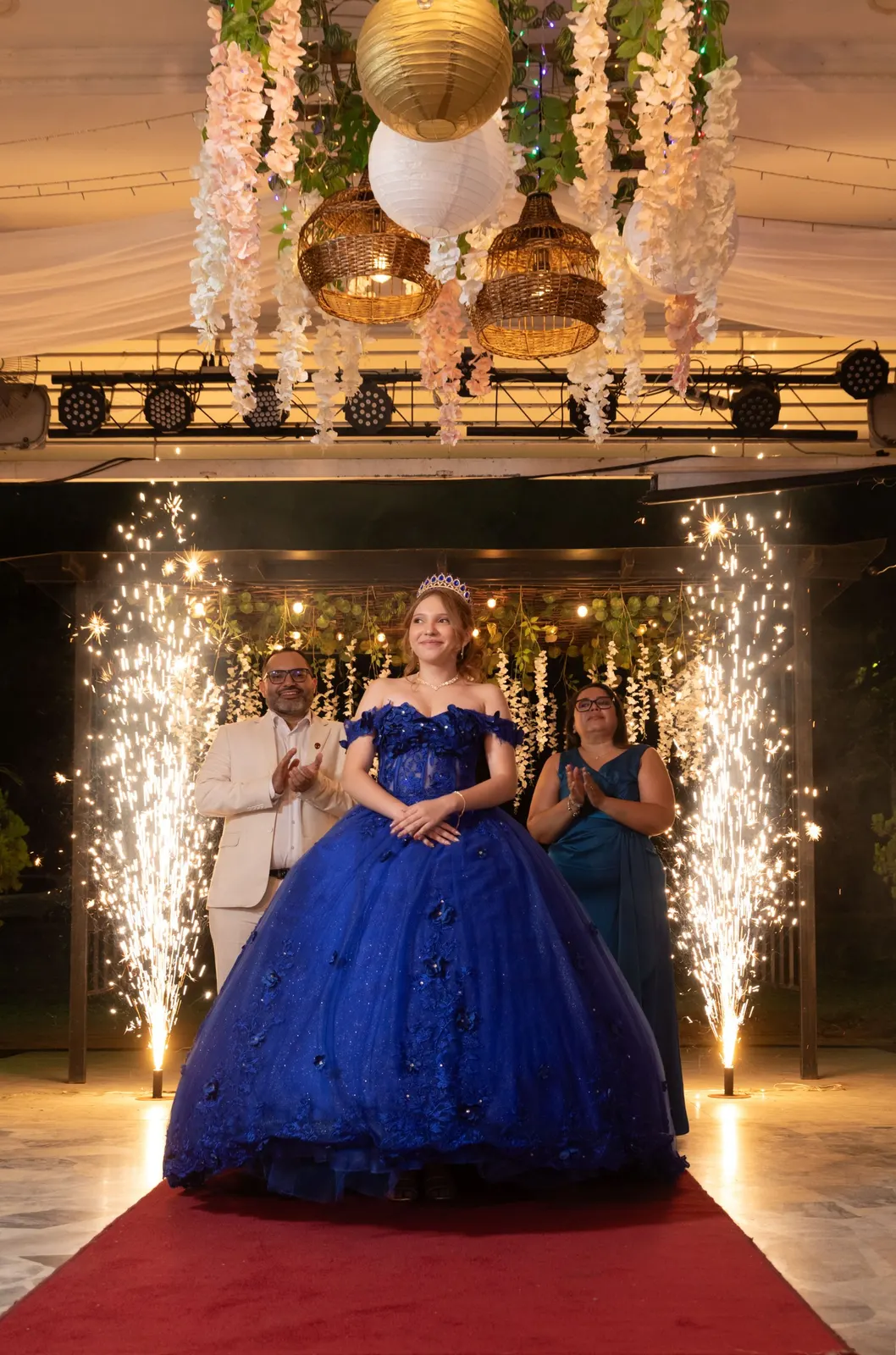 Quinceañera con vestido azul entrando entre chispas frías junto a sus padres