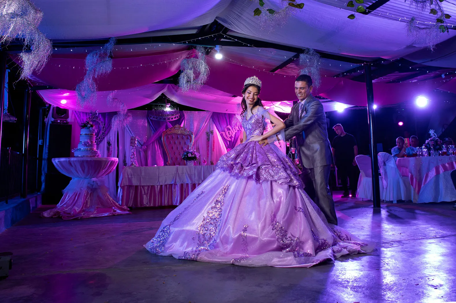 Quinceañera bailando con su padre bajo luces moradas