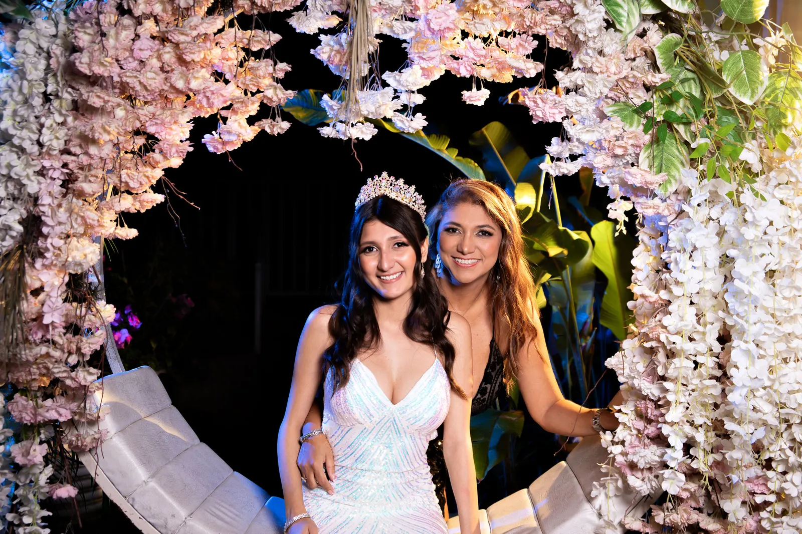 Quinceañera junto a su madre bajo un arco de flores