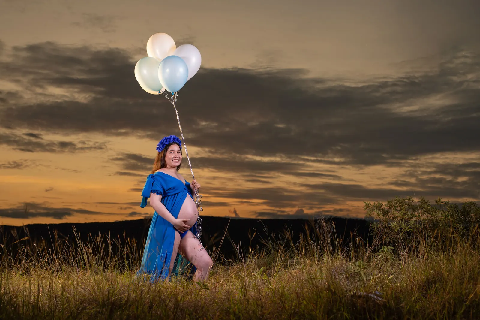 Mujer embarazada con vestido azul y globos al atardecer