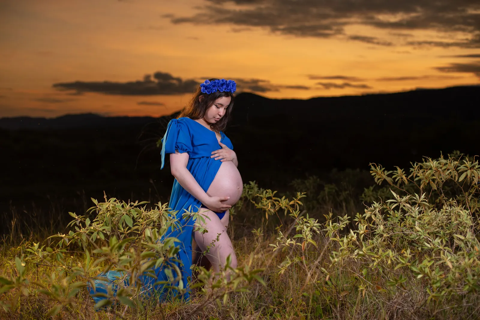 Mujer embarazada con vestido azul acariciando su vientre al atardecer