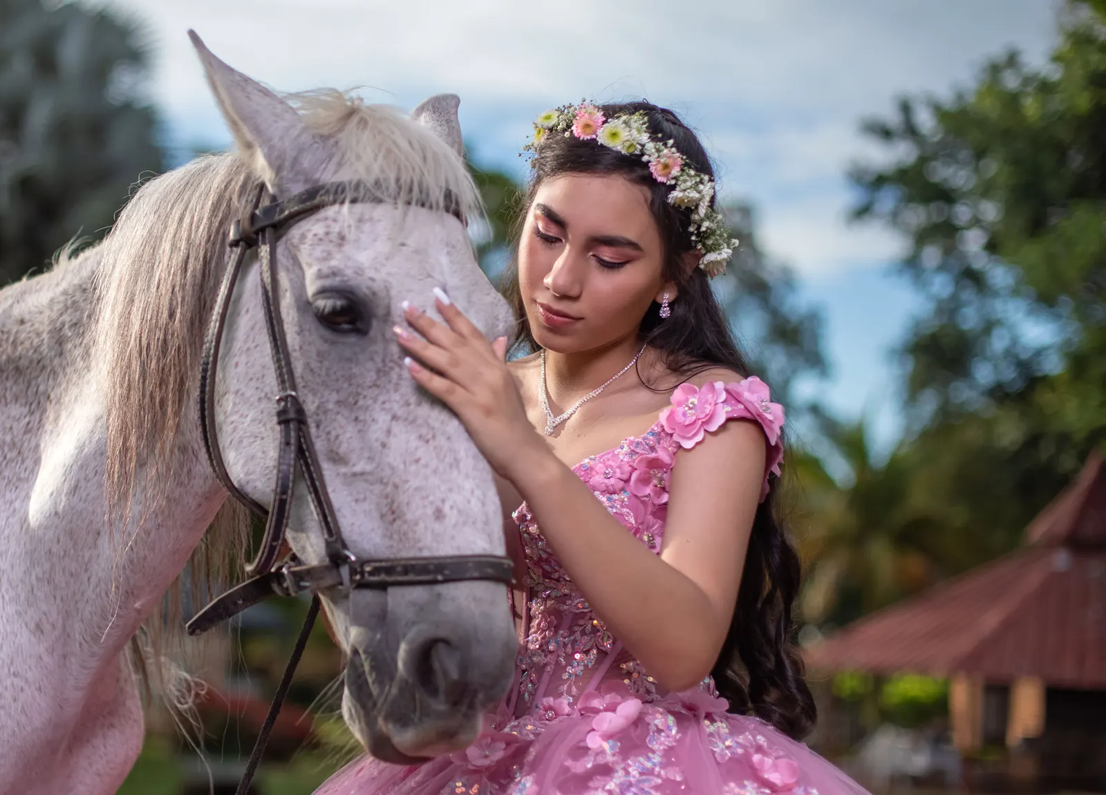 Quinceañera acariciando un caballo blanco con corona de flores
