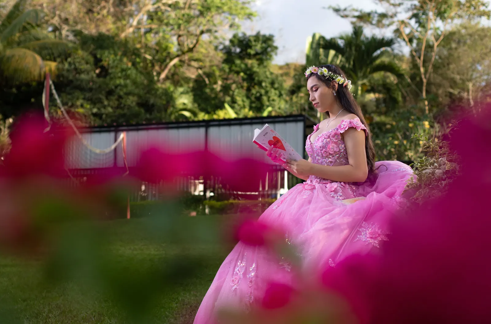 Quinceañera leyendo un libro entre flores de buganvilia