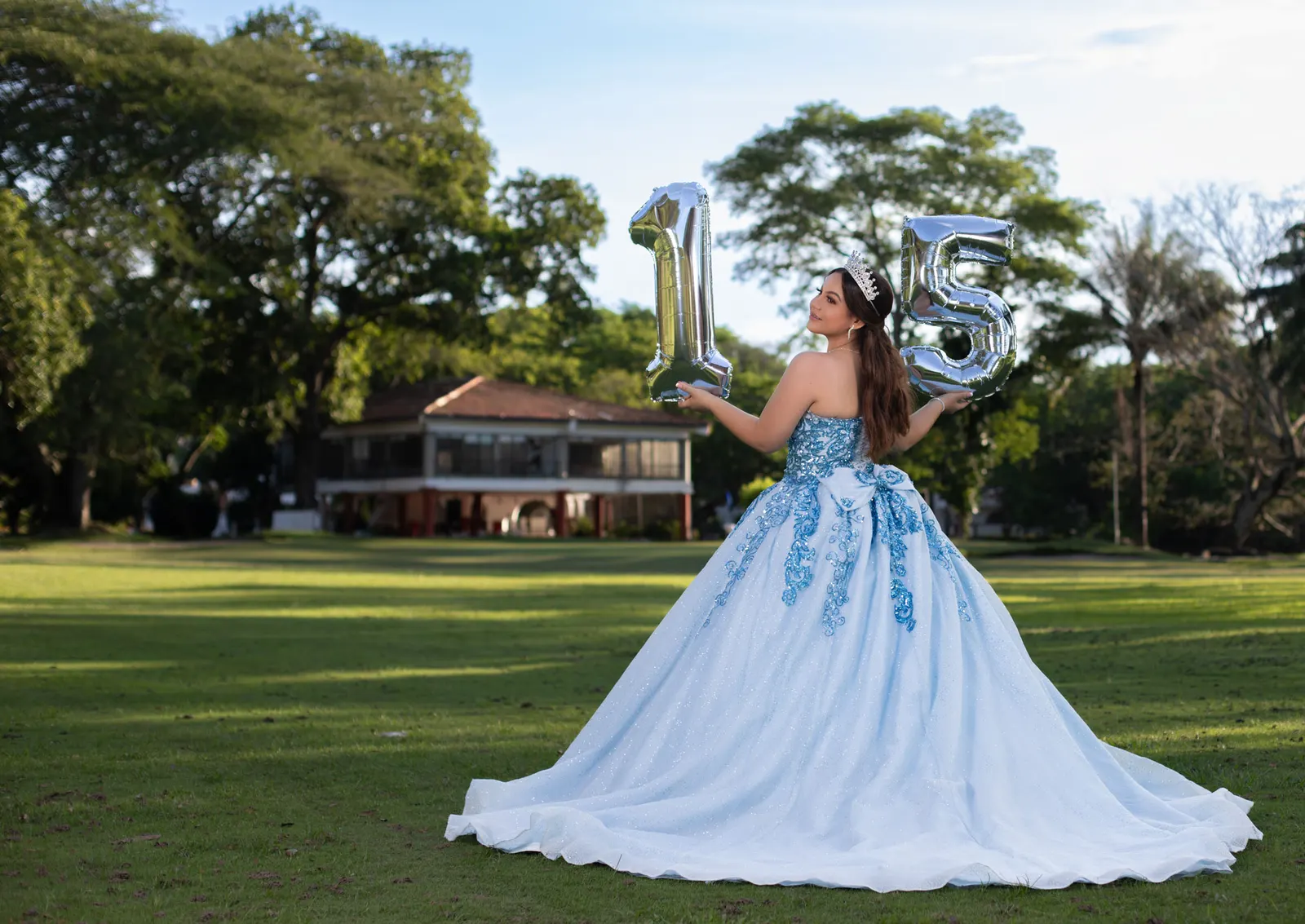 Quinceañera de espaldas con vestido azul y globos 15 en el parque
