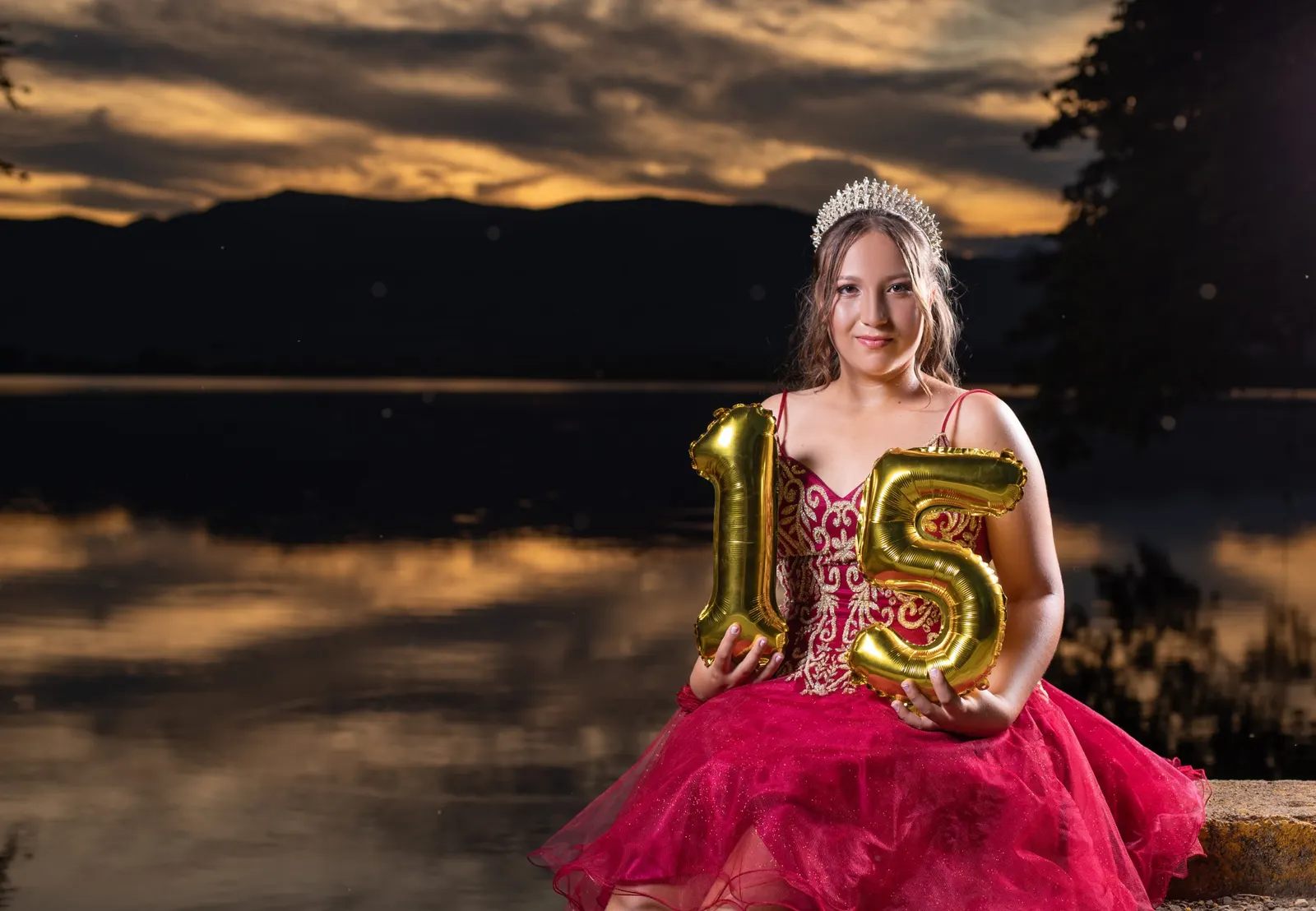 Quinceañera con globos dorados 15 sentada junto al lago