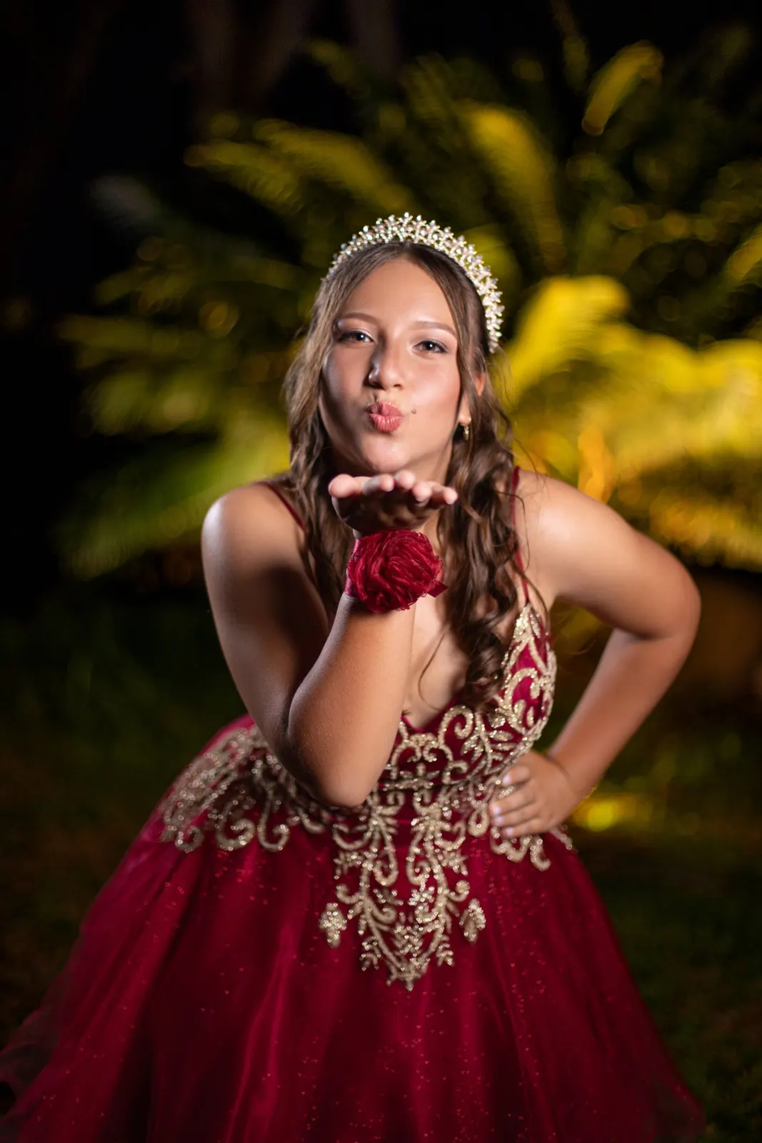 Quinceañera enviando un beso con vestido rojo y dorado
